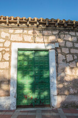 old green iron door in stone facade of a rural house in a village in Albacete