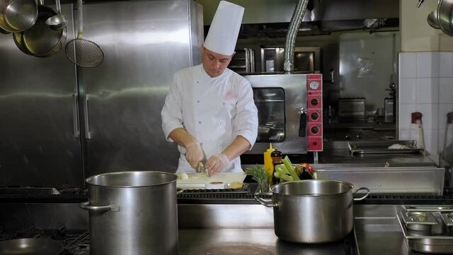 Portrait of a professional chef in the kitchen of a restaurant, he quickly cuts onions. A male chef in a white uniform is working in the kitchen. Slow motion.