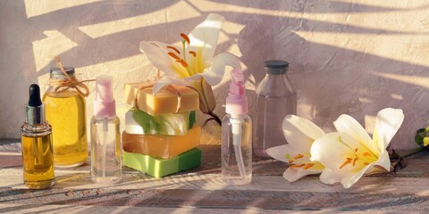 Soap, antiseptic spray and bottles with aromatic oil, white lily flower on a wooden background, natural cosmetics for home body care, banner