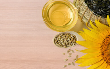 Sunflower oil, seeds and flowers of sunflower close up with space for text on wooden background.