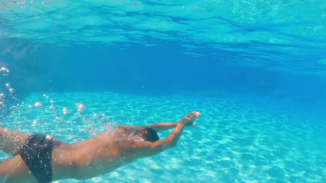 Underwater shooting. Man dive in blue swimming pool.