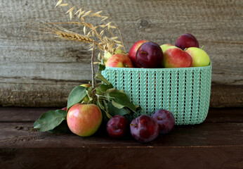 Fototapeta na wymiar Autumn still life. Ripe apples and plums, rye, wheat and oat ears. Autumn harvest in a basket on a wooden background.