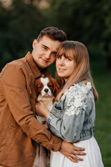 Naklejka na ściany i meble young happy couple standing near trees in the park and holding a dog
