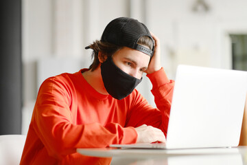 The man sits alone at a table in the open space, drinking coffee and working on his laptop. Freelance concept