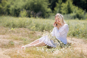 Fototapeta na wymiar Young white woman with blondy hair dressed in a white dress in summer in a field