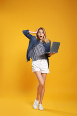 Full length portrait of emotional woman with modern laptop on yellow background