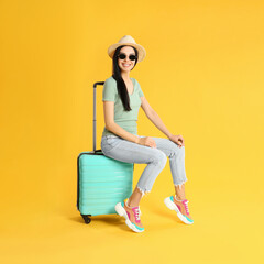 Beautiful woman with suitcase for summer trip on yellow background. Vacation travel