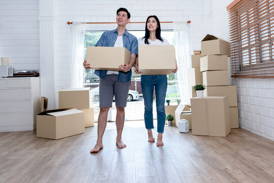 Asian Couple, Husband And Attractive Wife Helping Each Other To Lift The Box Happily, To Move Into A New Home For Starting A Marriage And Family Life.