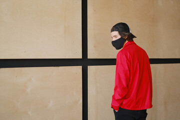 Fototapeta na wymiar Portrait of a young man 25-30 years old in a black protective mask, black cap and red jacket. 