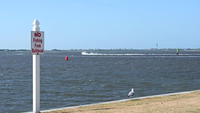 Looking over the bulkhead at the Cape fear river in Southport NC. A no fishing sign, a bird and a boat are in view.