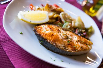 delicious salmon steak with potato garnish with slice of lemon on white plate in restaurant
