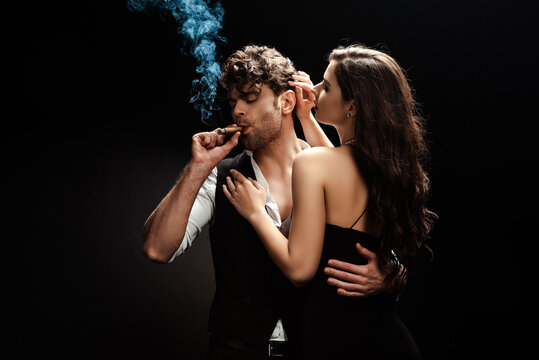 Man smoking cigar and embracing girlfriend on black background