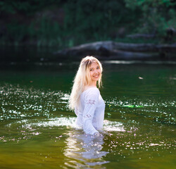 Young white woman with long blondy hair in a river in a forest in summer