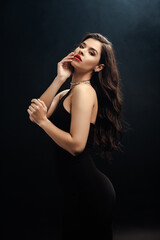 Naklejka premium sexy woman in black dress looking at camera on black background