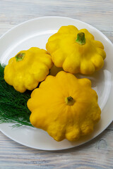 Three yellow round zucchini on a plate close-up. Fresh mini patty pan squash on a wooden table, selective focus