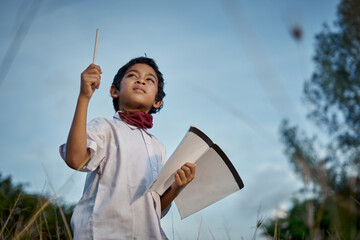 Portrait of an attractive schoolboy holding book and pen ready to study at natural park. New Normal Education concept