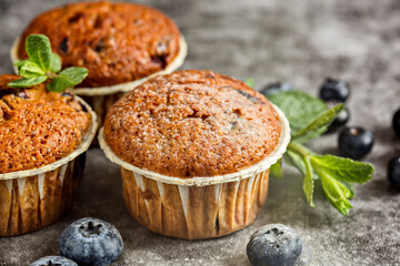 Several fragrant muffins with blueberries are on the table, next to blueberries and mint.