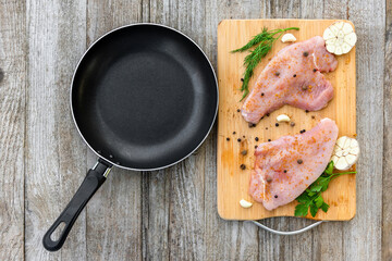 Raw Turkey steak is on a chopping Board with seasoning. On a wooden table