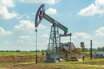 Oil pump in the field, beautiful blue sky with clouds. Russian oil production