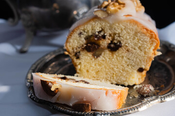 primer plano de budín con almendras y nueces y glacesado con elementos de plata tetera azucarera sobe mantel blanco con fondo oscuro