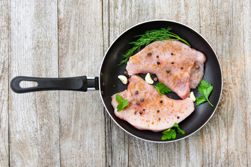 Raw steak with seasonings is in a frying pan on a wooden table