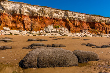 A view past sea eroded boulders towards a chalk rock fall at the base of the white, red and orange...