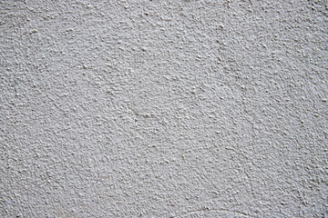 White plaster painted wall with grain and noise. Cracked wall closeup photo. Architecture detail background. Empty concrete wall. Grungy surface of painted cement. Abstract grainy texture