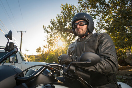 Image of a man in vintage style motorcycle helmet and goggles at dusk with trees and sun in background