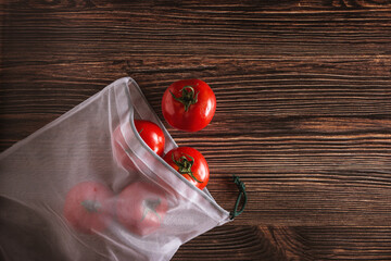Set of fresh tomatoes in a reusable shopping mesh bag on dark wooden background.  Ecological planet care concept.