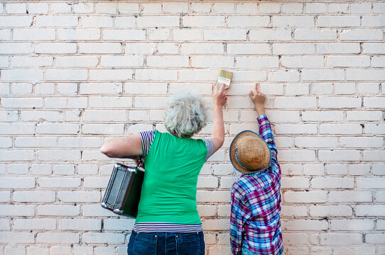 A boy and an elderly woman paint with a brush on a brick wall. Grandmother with a suitcase and grandson write an inscription on the wall. Space for an inscription. Blank for advertising