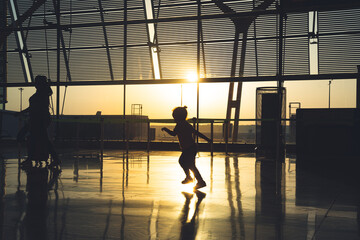 silhouette of an unrecognizable  child running through the airport terminal at sunrise.