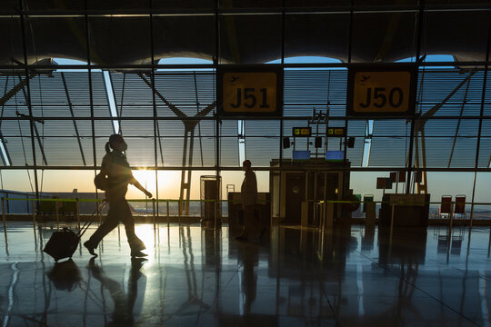 Silhouette of an unrecognizable woman with her suitcase at the airport in the departure terminal at sunrise.
