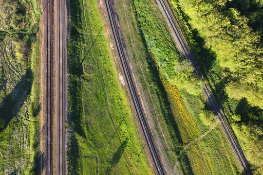 Aerial view of railways in countryside. Railroad tracks with grass and trees, top view. Transport infrastructure