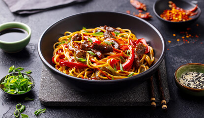 Stir fry noodles with vegetables and beef in black bowl. Slate background. Close up. - obrazy, fototapety, plakaty
