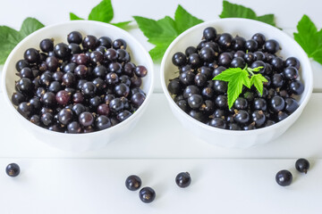 fresh black currant berries in white bowls close-up. white background with black currant berries.