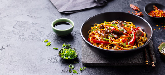 Stir fry noodles with vegetables and beef in black bowl. Slate background. Copy space.