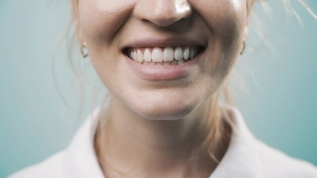 Smiling female mouth with natural white teeth, selective focus. Close up smiling woman face with perfect smile in light blue background. Smile healthy teeth concept, 4k