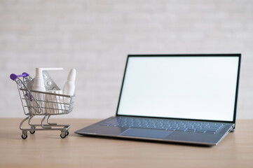 Laptop with blank white screen and miniature shopping cart full of medicines. Online pharmacy concept. Website for buying tablets.