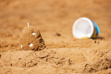 A sandcastle on a sandy beach, set against a bright blue summer sky.