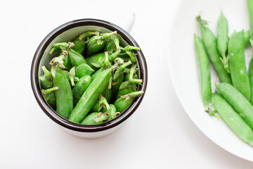 Green peas in a white metal mug and on a plate. Selective focus