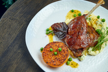 Appetizing confit duck leg with grilled orange and mashed potato garnish on a white plate on a wooden background