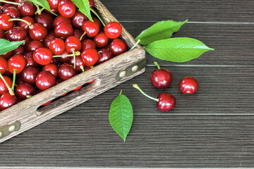 ripe cherry berries in a wooden box on a wooden background close-up. background with ripe cherries and green leaves.