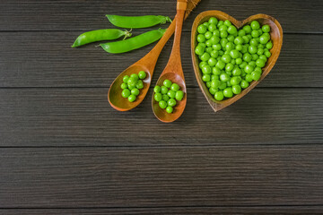 fresh peas peeled from pods in a wooden plate and wooden spoons on a wooden background top view. background with sweet green peas in a bowl and a copy of the space. 