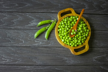fresh peas peeled from pods in a wooden plate and spoon on a wooden background top view. background with sweet green peas in a bowl and a copy of the space. fresh peeled peas view above.