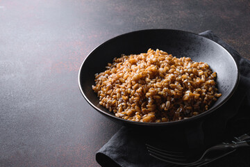 Cooked Whole Grain cereal spelt with butter in black bowl on dark brown background. Close up.