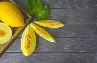 fresh ripe yellow melon in a wooden box and melon slices on a wooden background above. wooden background with whole melon and melon slices. melon close-up on the table.