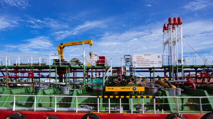 Pipelines system with crane on crude oil tanker during maintenance at shipyard against white clouds and blue sky background