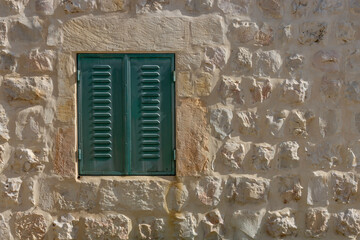 A Green metal window blind, in a stone wall typical of Jerusalem, Israel