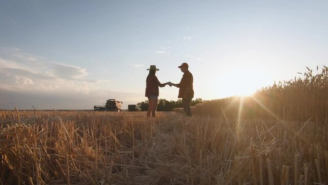 Farmers handshake over the wheat crop in harvest time. Team farmers stand in a wheat field with tablet at sunset. Partnership concept.