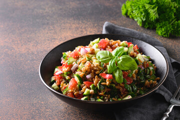 Cooked Whole Grain cereal spelt salad with seasonal vegetables in bowl on brown background. Close up.
